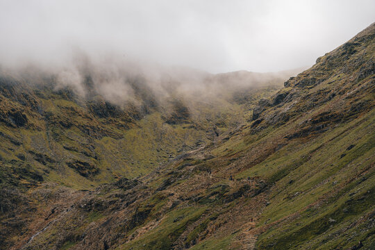 View of Y Lliwedd mountain ridge with rocky slopes, green grass, and low-hanging clouds in Caernarfon, Wales, United Kingdom.