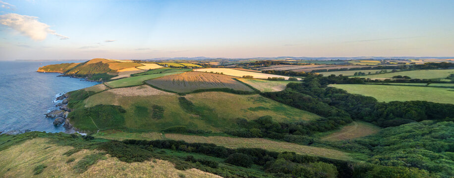 Aerial view of Lansallos Beach featuring rolling green hills, agricultural fields, and rugged coastline under a clear sky in Looe, Cornwall, United Kingdom.