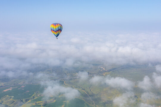 Aerial view of a colorful hot air balloon floating above a landscape of green fields and scattered clouds in Kibbutz Ruhama, South District, Israel.