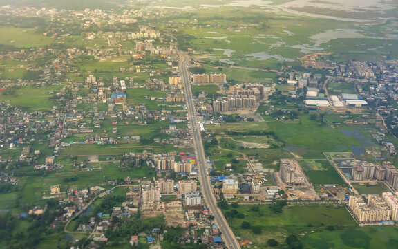 Aerial view of the Airport Exit Road surrounded by residential buildings, lush green fields, and wetlands in Guwahati Kahikuchi, Assam, India.