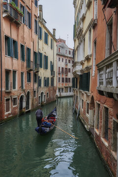 Venice, Italy - 06 May 2022: View of a gondolier rowing a traditional gondola through a narrow canal lined with historic buildings in Venice, Veneto, Italy.