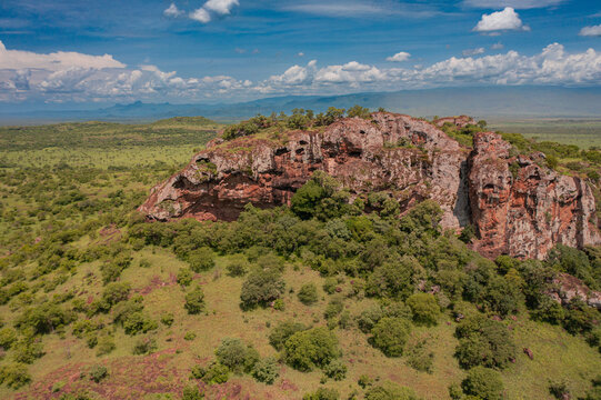 Aerial view of the rugged red rock formations of Pian Upe Game Reserve surrounded by lush green savanna and scattered trees in Namalu, Northern Region, Uganda.