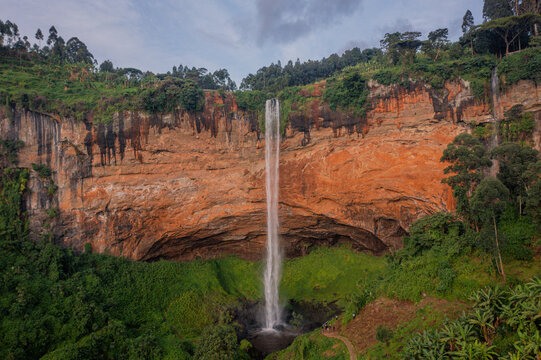 Aerial view of Sipi Falls cascading down a dramatic orange-hued cliff face surrounded by lush green vegetation and trees in Kapchorwa, Eastern Region, Uganda.
