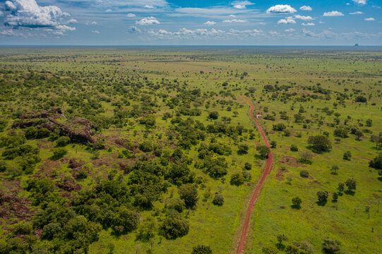 Aerial view of Pian Upe Game Reserve featuring vast savanna grasslands, scattered acacia trees, rocky outcrops, and a red dirt road winding through the landscape in Namalu, Northern Region, Uganda.
