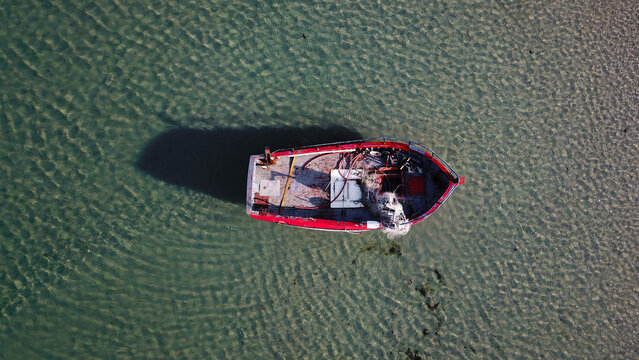 Aerial view of a small red fishing boat floating in the clear shallow waters of the Atlantic Ocean near Penvins, Sarzeau, Bretagne, France.
