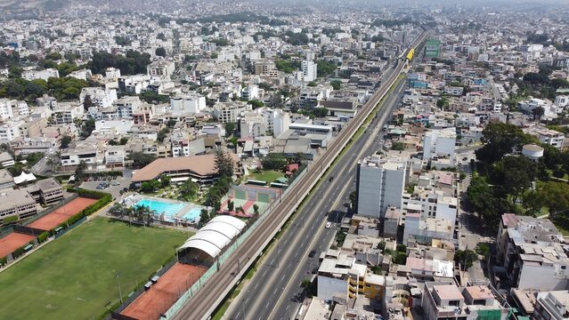 Aerial view of the urban landscape featuring the Ovalo Higuereta area, elevated train tracks, dense residential buildings, and sports facilities in Santiago de Surco, Provincia de Lima, Peru.