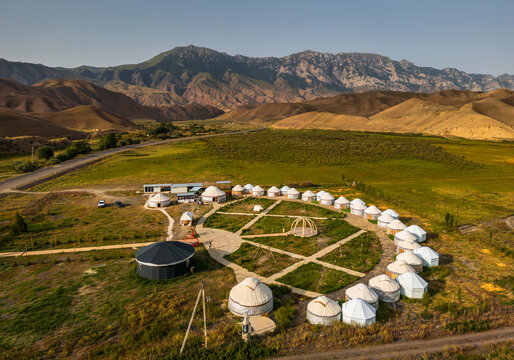 Aerial view of a traditional yurt camp nestled in a vast valley surrounded by rugged mountains under a clear sky in Naryn, Naryn Region, Kyrgyzstan.