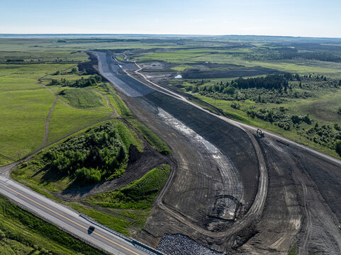 Aerial view of the Elbow River construction site featuring earthworks and infrastructure development amidst green fields in Calgary, Alberta, Canada.