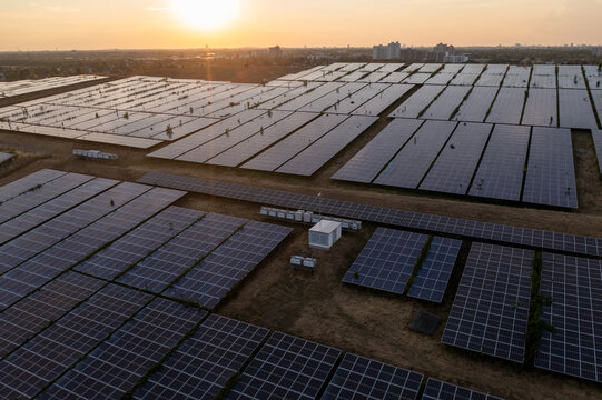 Aerial view of a large solar farm with rows of photovoltaic panels at sunset, featuring the Berlin skyline and TV tower in the distance in Schonefeld, Brandenburg, Germany.