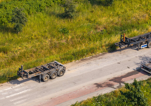 Aerial view of two empty truck trailers parked on the side of a rural road surrounded by lush green vegetation in Gdansk, Pomeranian Voivodeship, Poland.