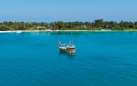 Aerial view of a Sri Lankan fishing boat anchored in the turquoise waters of the lagoon with a lush tropical island coastline in the background in Vaanee, Dhaalu Atoll, Maldives.