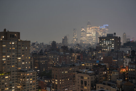 New York, United States - 15 July 2026: View of the illuminated Manhattan skyline at dusk with residential buildings in the foreground and glowing skyscrapers under a twilight sky.