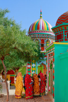 View of a vibrant, colorfully decorated shrine with intricate patterns and a dome, with women in traditional clothing standing in front, in Islamkot, Sindh, Pakistan.
