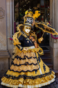 Riquewihr, France - 04 July 2026: View of a person wearing an elaborate gold and black Venetian carnival costume with an ornate mask and matching parasol standing in front of a shop entrance.