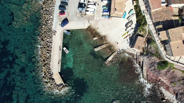 Aerial view of Mallorca cove with small boats, kayaks, and a concrete ramp in the clear turquoise water of the Mediterranean Sea in Balearic Islands, Spain.