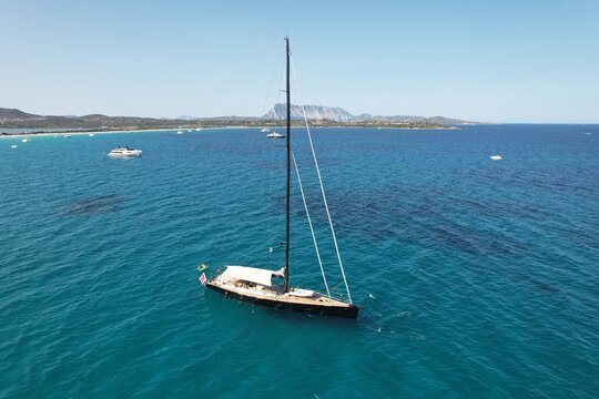Aerial view of a sleek sailboat anchored in the clear turquoise waters of the Mediterranean Sea off the coast of Sardinia, Italy.