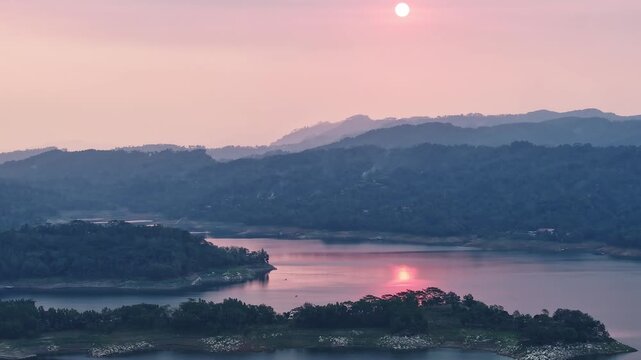 Aerial view of Wadaslintang Reservoir at sunset with golden light reflecting on the water and rolling hills in the background in Wadaslintang, Central Java, Indonesia.