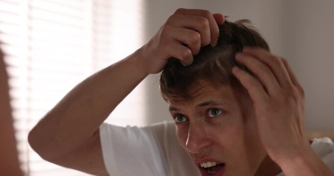 Dandruff problem. Worried man examining his head near mirror at home. Camera moving forward