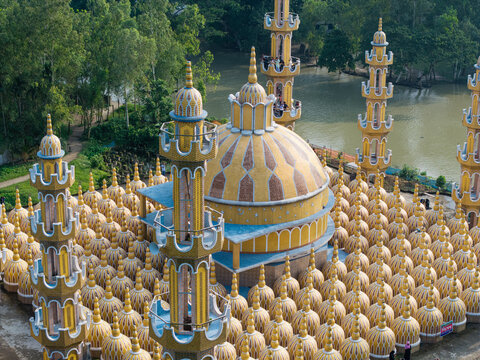Tangail District, Bangladesh - 17 July 2026: Aerial view of 201 Gombuj Masjid with its distinctive yellow domes and tall minarets, surrounded by lush green trees and a nearby river.