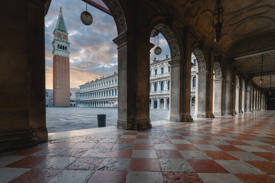 View of the historic Piazza San Marco and the iconic Campanile di San Marco seen through the elegant arches of the Procuratie Nuove at sunset in Venezia, Veneto, Italy.