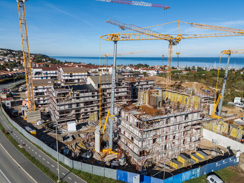 Aerial view of a construction site with multiple yellow tower cranes, unfinished apartment buildings, and scaffolding near the Adriatic Sea in Izola, Izola, Slovenia.