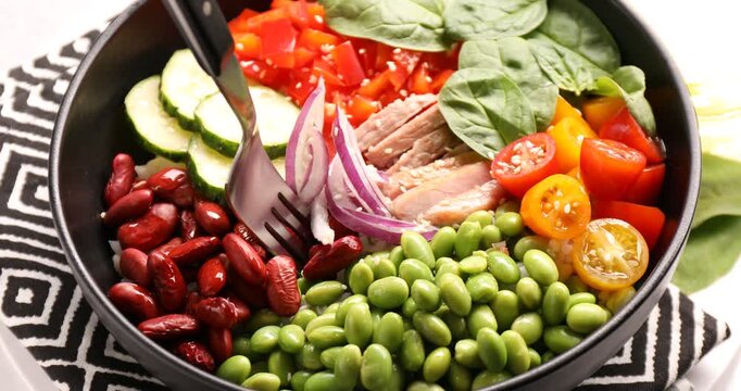 High fiber food. Taking tasty salad, meat and sesame seeds from bowl at light table, closeup