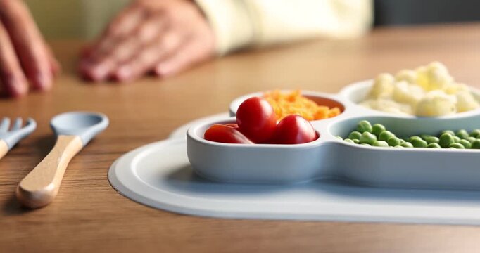 Baby tableware. Woman putting cutlery near section plate with food at wooden table, closeup
