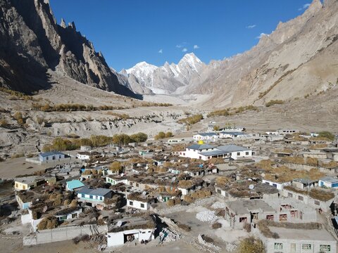 Aerial view of Siachen Glacier with a remote mountain village featuring stone houses and flat roofs surrounded by rugged peaks and arid landscape in Pakistan.