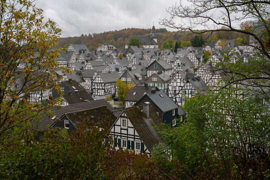 View of traditional half-timbered houses with slate roofs and a church spire nestled among trees in Germany.