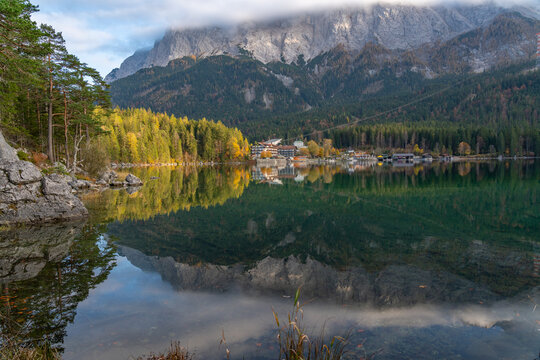 View of Eibsee lake with reflections of the Zugspitze mountain, surrounded by pine trees and autumn foliage in Germany.