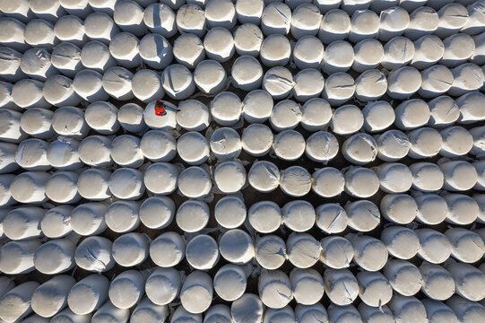 Karaman Merkez, Turkiye - 09 September 2024: Aerial view of white plastic-wrapped hay bales arranged in rows on a field near Kilbasan Yolu, with a person in a red jacket standing among them.