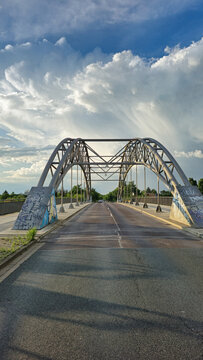 View of the Holzwiesenbrucke steel arch bridge with graffiti-covered concrete supports under a dramatic cloudy sky in Hannover, Niedersachsen, Germany.