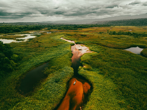 Aerial view of the winding river in Chapada Diamantina with lush green wetlands and a small boat navigating the calm waters in Andarai, State of Bahia, Brazil.