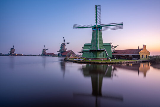 View of traditional green windmills reflected in the calm water of a canal at dusk in the Netherlands.