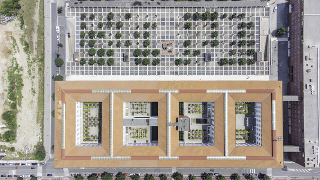 Aerial view of the Bicocca district featuring a large rectangular building with terracotta roofs and internal courtyards next to a grid-patterned square with trees in Milan, Lombardy, Italy.