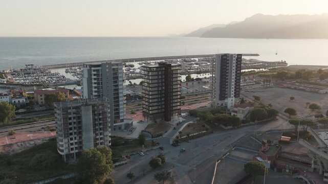 Salerno, Campania, Italy - 18 July 2026: Aerial view of the Arechi Stadium area, featuring modern residential buildings, a nearby marina with boats, and the coastline under a soft sunset light.