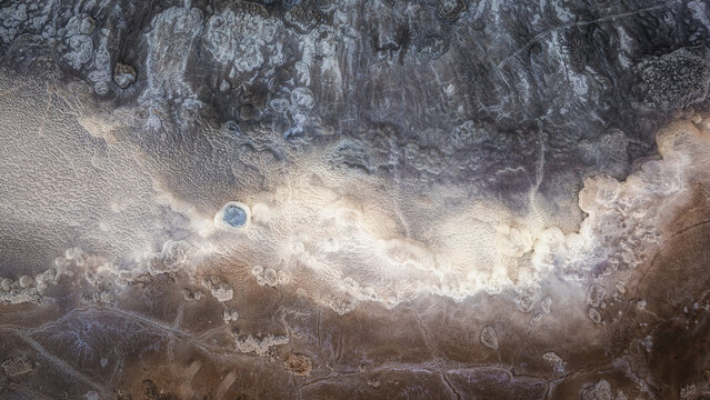 Aerial view of Hveravellir geothermal area with mineral-rich pools, textured volcanic soil, and steaming vents in Hunabyggd, Iceland.