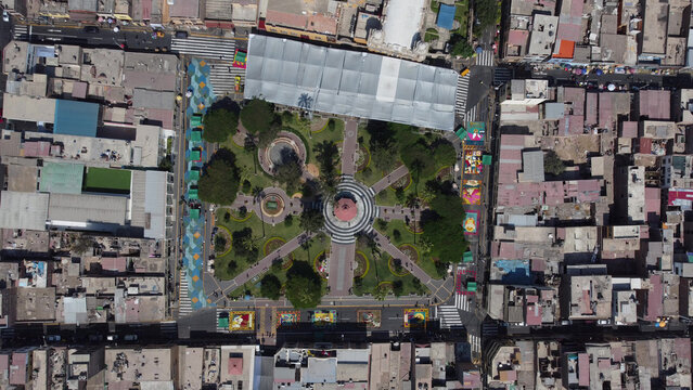 Aerial view of the main square in Surco District during Holy Week, featuring floral carpets, a central gazebo, and surrounding urban buildings. Surco District, Lima Region, Peru.