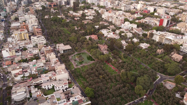 Aerial view of El Olivar de San Isidro Park featuring lush olive trees, a central pond, and surrounding urban residential buildings in Lima, Provincia de Lima, Peru.