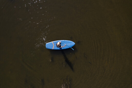 Aerial view of a person paddling on a blue stand-up paddleboard in calm dark water in Oriola, Distrito de Evora, Portugal.