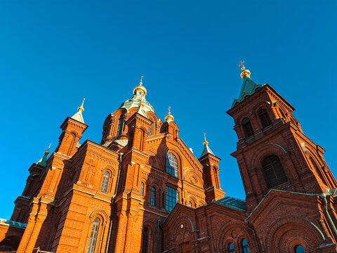 View of Uspenski Cathedral, a historic red-brick Eastern Orthodox church with golden domes under a clear blue sky in Helsinki, Uusimaa, Finland.