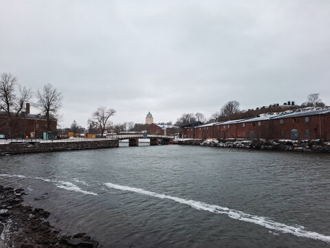 Helsinki, Finland - 02 January 2026: View of Suomenlinna fortress with historic red brick buildings and a bridge over the water under a cloudy winter sky.