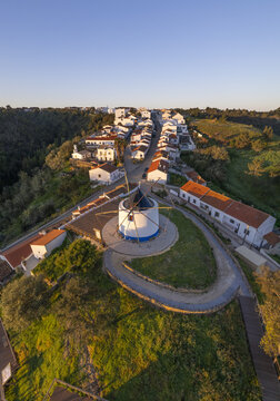 Aerial view of Odeceixe windmill overlooking white houses at sunset with golden light on rooftops and green hills Odeceixe, Faro District, Portugal.