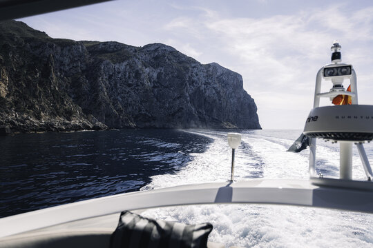 Mallorca, Spain - 20 April 2024: View of a boat cruising along the rugged limestone cliffs of the Mallorca coastline under a bright blue sky.