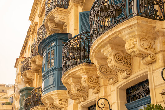 Valletta, Malta - 15 July 2022: View of traditional Maltese balconies with ornate stone corbels and blue wooden shutters on a historic limestone building in Valletta, Malta.
