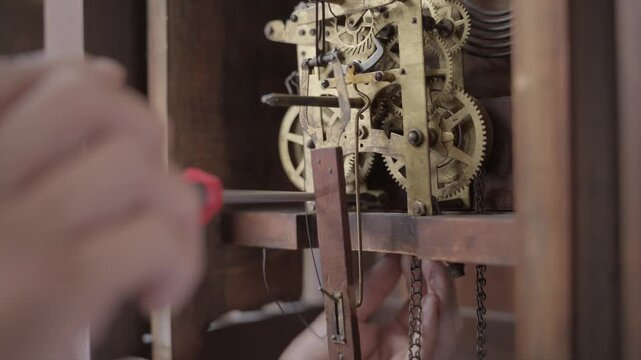 Profile close up shot of a watchmaker using a precision manual screwdriver to adjust and tighten gears inside an antique mechanical grandfather clock.