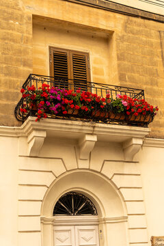 Valletta, Malta - 15 July 2022: View of a traditional balcony adorned with vibrant red and purple geraniums on a historic limestone building facade.