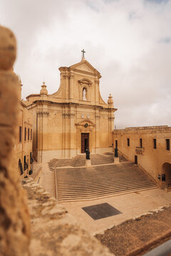 Valletta, Malta - 15 July 2022: View of the Cathedral of the Assumption featuring a grand stone staircase and historic limestone facade under a cloudy sky.