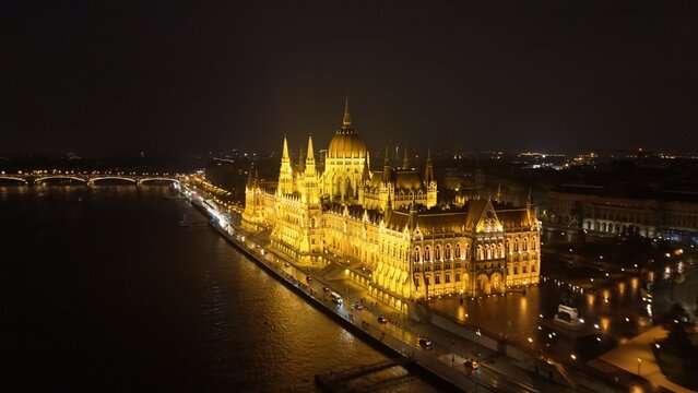 Aerial view of the illuminated Hungarian Parliament Building along the Danube River at night in Budapest, Hungary.