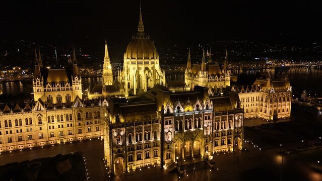 Aerial view of the illuminated Hungarian Parliament Building at night, featuring its intricate Gothic Revival architecture and glowing facade along the Danube River in Budapest, Hungary.